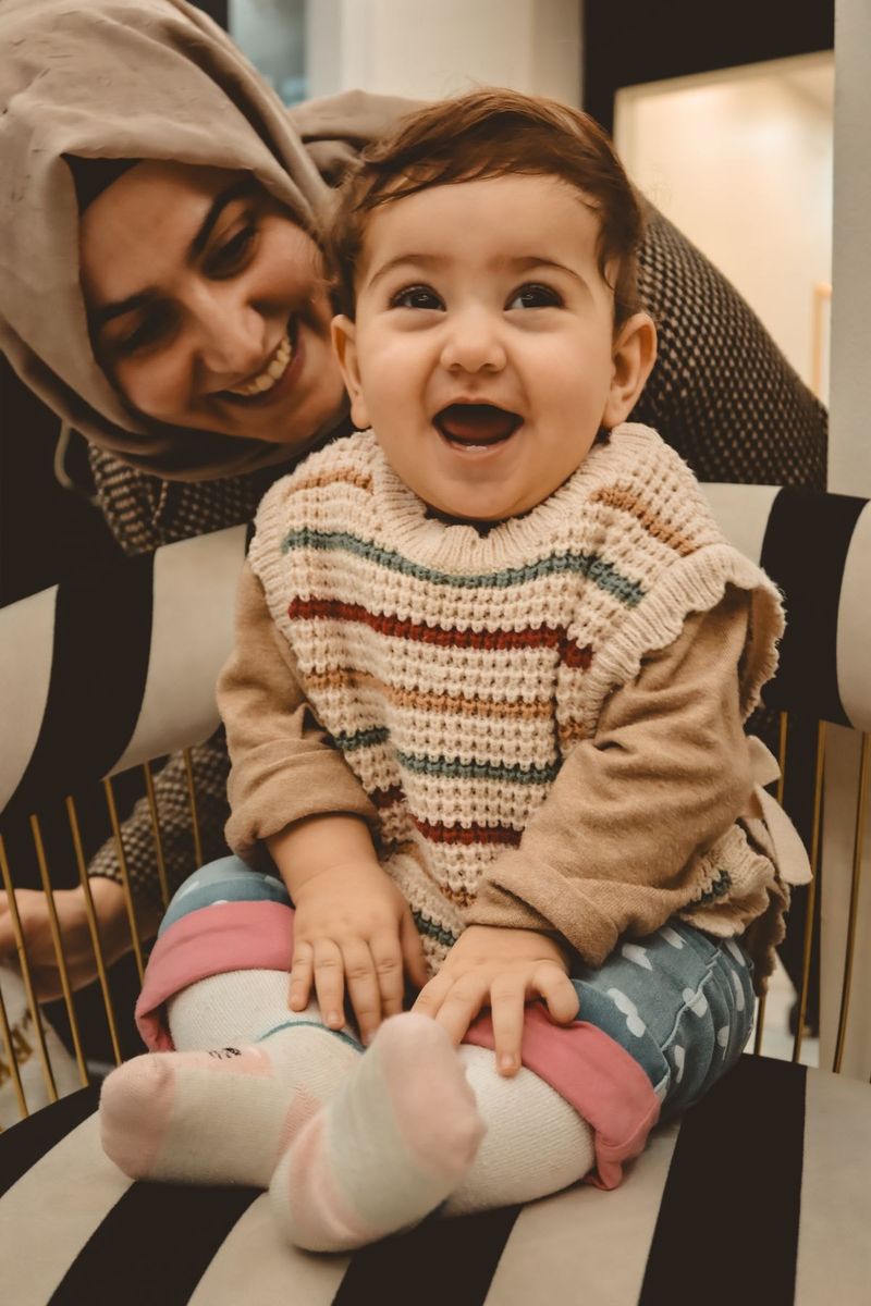 A mother in a cream headscarf smiles down at her laughing baby.