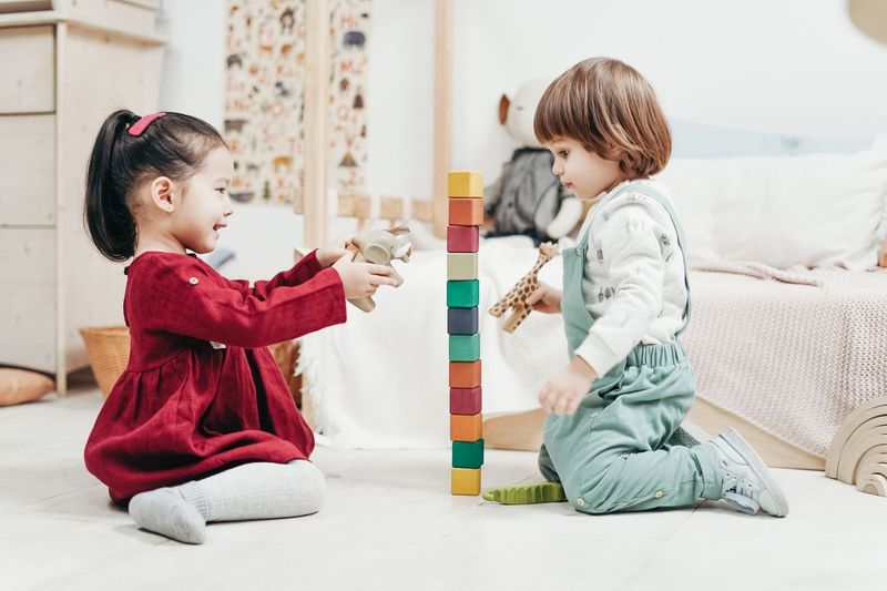 Two toddlers building a tall tower of colourful wooden blocks together.