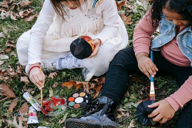 Two children painting together on a woodland floor covered in autumn leaves.