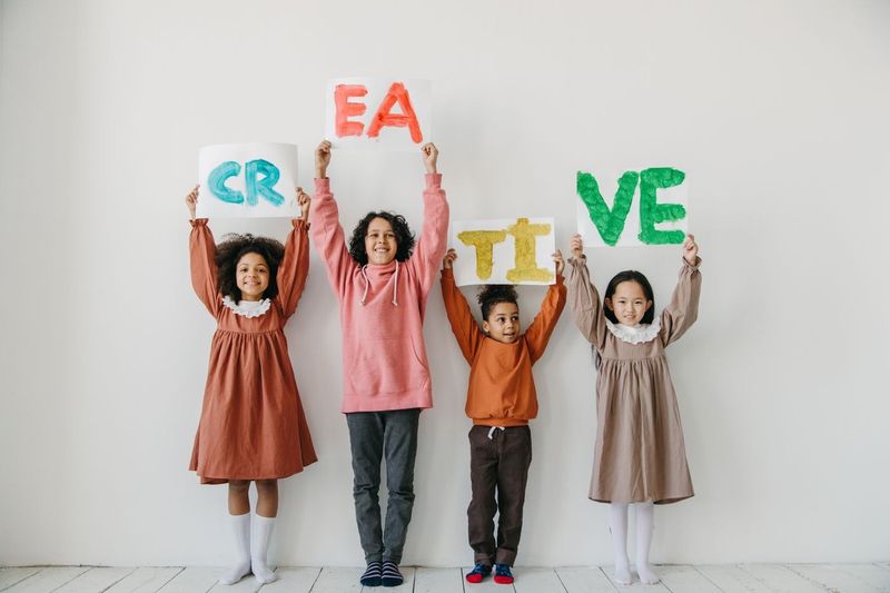 Four children in autumn-coloured clothes holding up paper letters that spell CREATIVE.