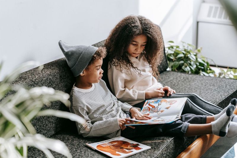 Two children sharing a picture book on a sofa.