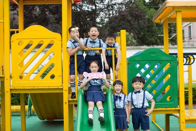 A group of smiling children standing on a yellow and green play structure beside a slide.